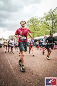 Runner in a red shirt leads a race on a city street, bib 52993, with other runners behind him.
